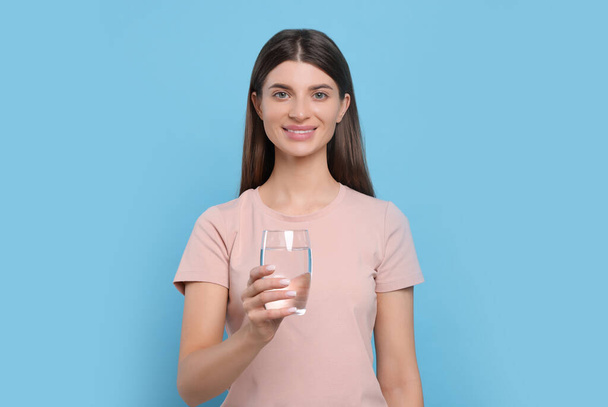 Healthy habit. Portrait of woman holding glass with fresh water on light blue background - Foto, Imagen