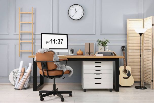 Stylish workplace with computer, houseplant and stationery on wooden desk near grey wall at home - Photo, Image