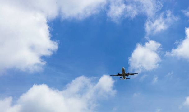 Коммерческая авиакомпания, летающая на голубом небе и белых облаках. Под видом летающего самолета. Пассажирский самолет, летящий в голубом небе с красивыми белыми пушистыми облаками. - Фото, изображение