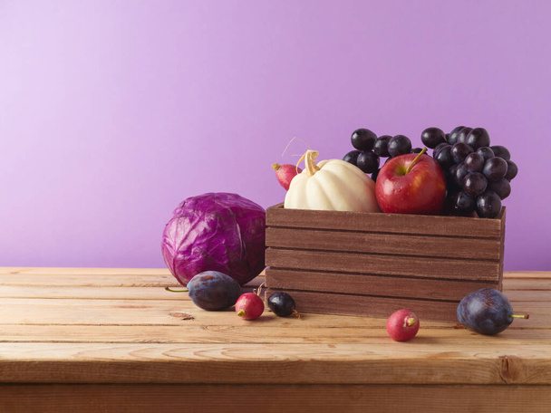 Autumn harvest concept.  Pumpkin, apple, grapes and vegetables in wooden box on table over purple background - Φωτογραφία, εικόνα