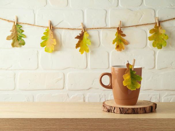 Coffee cup on wooden table over brick wall background with autumn leaf garland - Fotografie, Obrázek