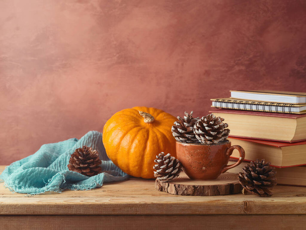 Autumn concept with pine cone in coffee cup, pumpkin and books on wooden table. Thanksgiving greeting card - Foto, Imagem