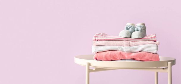 Stack of baby clothes and socks on table against lilac background with space for text - Фото, изображение