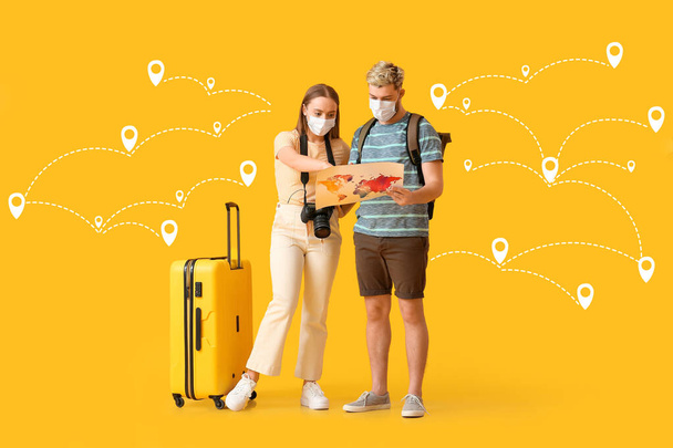 Pareja de turistas en máscaras, con maleta y ruta dibujada con punteros de ubicación sobre fondo amarillo - Foto, imagen