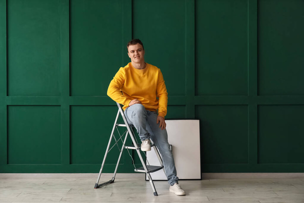 Mladý muž sedící na žebříku u zelené zdi - Fotografie, Obrázek