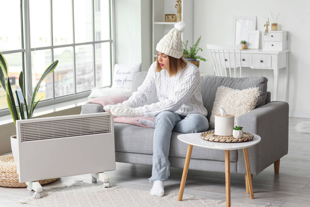 Frozen young woman in winter clothes warming near radiator at home - Photo, Image