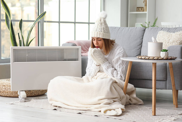 Frozen young woman in winter clothes warming near radiator at home - Photo, image