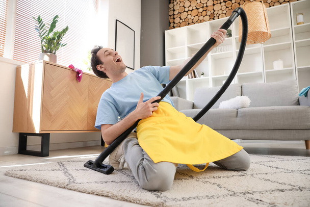 Young man having fun while hoovering his apartment - Фото, изображение