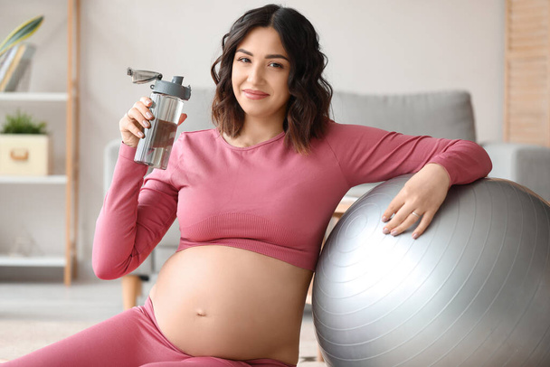 Sportos terhes nő egy üveg vízzel és fitball otthon - Fotó, kép