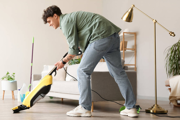 Young man with vacuum cleaner at home - Photo, Image