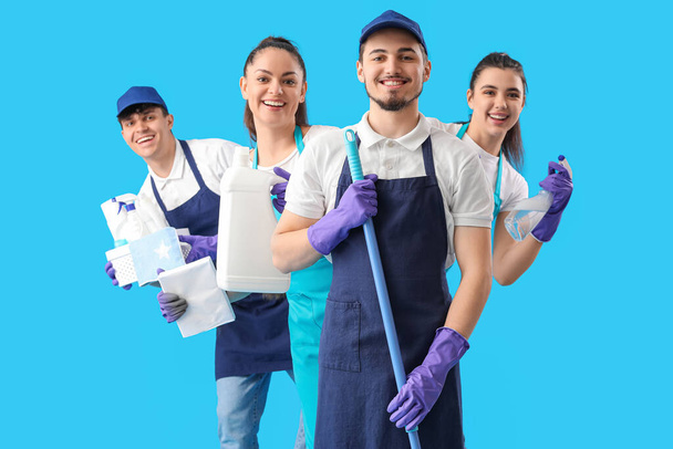 Young janitors with cleaning supplies on blue background - Фото, изображение