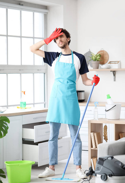 Zmęczony młody człowiek mycie podłogi w kuchni - Zdjęcie, obraz