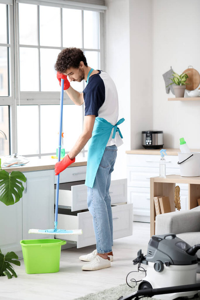 Young man mopping floor in kitchen - Fotó, kép