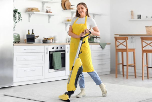 Giovane donna aspirapolvere tappeto in cucina - Foto, immagini