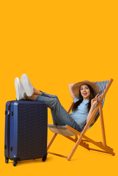 Молода жінка з валізою на стільці, що показує жест перемоги на жовтому тлі - Фото, зображення