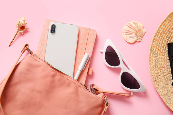 Stylish bag with mobile phone and different accessories on pink background - Foto, afbeelding