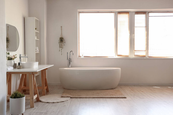 Interior del baño ligero con lavabo blanco, bañera y estantería - Foto, imagen