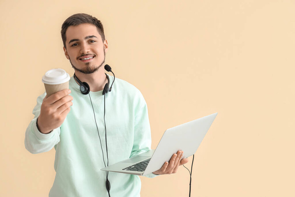 Agente de soporte técnico masculino con portátil y café sobre fondo beige - Foto, imagen