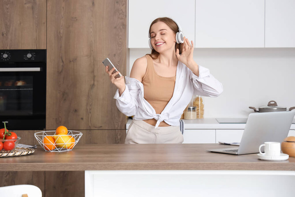 Mujer joven y feliz escuchando música y bailando en la cocina moderna - Foto, Imagen