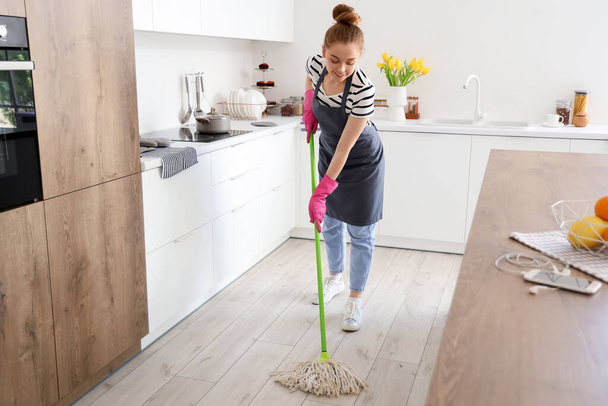 Pretty young woman mopping floor in light kitchen - Foto, afbeelding