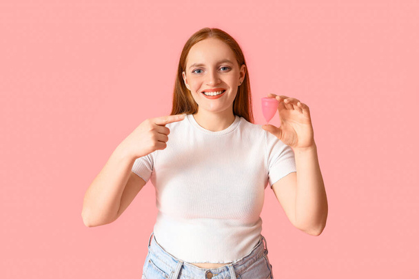 Mujer joven señalando la copa menstrual sobre fondo rosa - Foto, imagen