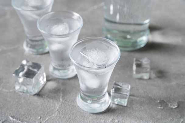 Shots and bottle of vodka with ice cubes on grey background - Foto, Bild