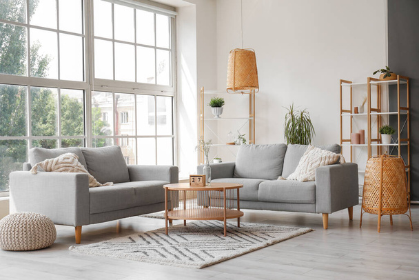 Интерьер светлой гостиной с серыми диванами, журнальным столиком и большим окном - Фото, изображение
