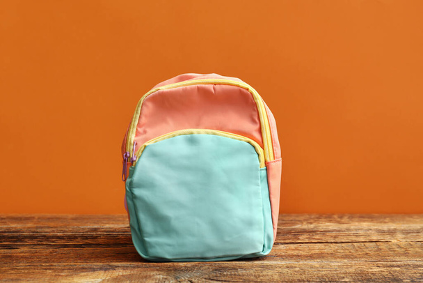 Kolorowy plecak szkolny na drewnianym stole przy pomarańczowej ścianie - Zdjęcie, obraz
