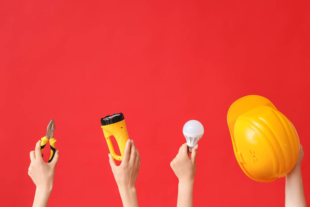 Electrician hands with tools and light bulb on red background - Valokuva, kuva