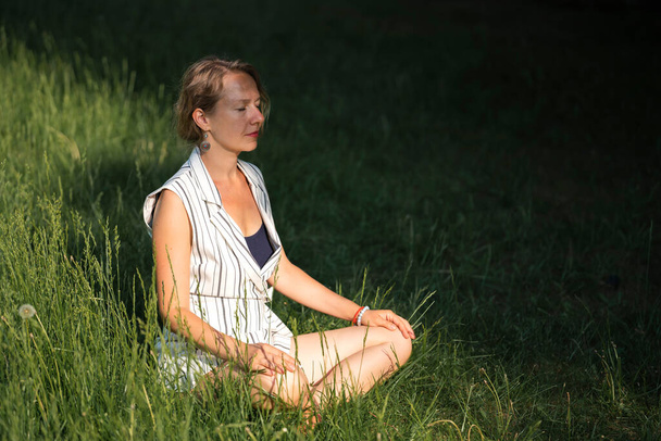 Een jonge blonde vrouw mediteert op het gras in het park tijdens een lunchpauze. Hoge kwaliteit foto - Foto, afbeelding