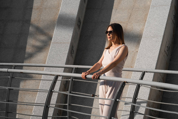 Urban zomer portret van jonge brunette vrouw. Een vrouw staat op een brug met een betonnen muur achter haar. Hoge kwaliteit foto - Foto, afbeelding