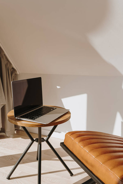 Luxusní minimální design interiéru. Světlé moderní skandinávské pracoviště s notebookem, koženým křeslem a stíny slunečního světla na stěně - Fotografie, Obrázek