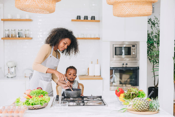 onnellinen afrikkalainen musta nuori äiti poikansa kanssa ihana söpö ruoanlaitto yhdessä kotona loma toimintaa - Valokuva, kuva
