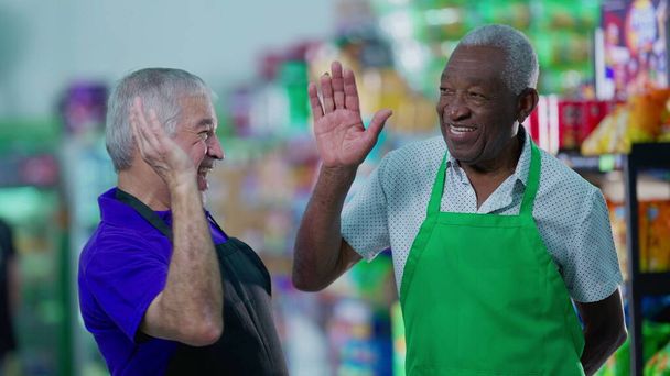 スーパーマーケットの通路に5階建てで成功を祝う幸せな多様な先輩従業員。アフリカ系アメリカ人の同僚と労働力のチームワークに従事する白人マネージャー - 写真・画像