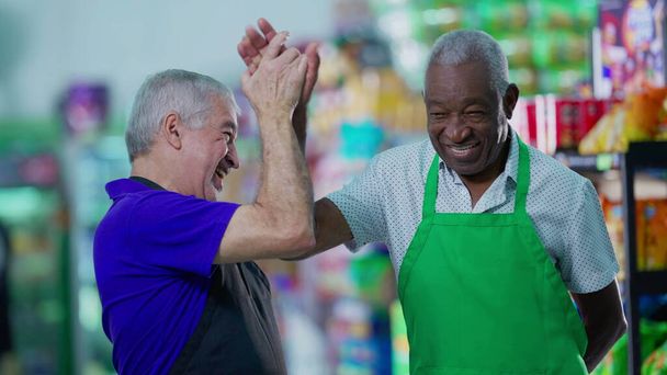 Gelukkige diverse senior medewerkers vieren succes met high-five staan in supermarkt gangpad. Kaukasische manager werkt samen met Afro-Amerikaanse collega - Foto, afbeelding