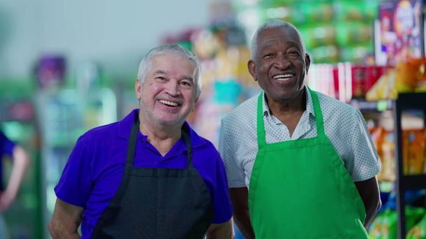 Szczęśliwie zróżnicowani starsi pracownicy świętują sukces przybijając piątkę w nawie supermarketów. Menedżer rasy kaukaskiej angażujący się w pracę zespołową z Afroamerykańskim kolegą - Zdjęcie, obraz