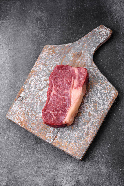 Friss nyers marhahús csíkos steak sóval, fűszerekkel és fűszernövényekkel sötét beton alapon - Fotó, kép
