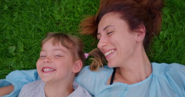 3 éves lány, anyával a zöld füvön a parkban nevetve. A boldog család a nyári parkban együtt pihen. Örökbe fogadott lány egy új anyával. A gyermekek örökbefogadásának fogalma. - Felvétel, videó