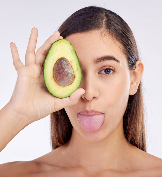 Face, skincare and woman with avocado, tongue out and isolated on a white background in studio. Portrait, beauty and natural model with fruit food for nutrition, healthy diet or omega 3 for wellness. - Photo, Image