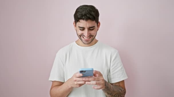 Jonge Spaanse man met behulp van smartphone doen duim omhoog gebaar over geïsoleerde roze achtergrond - Video