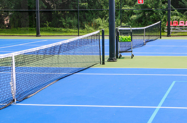 Sivunäkymä sininen ja vihreä tenniskenttä kärry täynnä tennispalloja suljettu musta miekkailu. - Valokuva, kuva