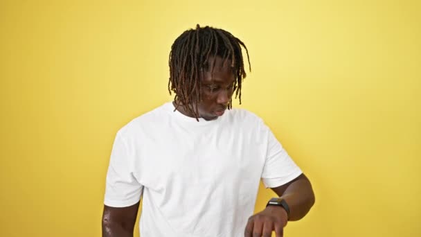Αφροαμερικάνος στέκεται με έκφραση έκπληξη looing ρολόι πάνω από απομονωμένο κίτρινο φόντο - Πλάνα, βίντεο