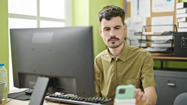 Fiatal spanyol férfi üzleti dolgozó számítógép és okostelefon dolgozik az irodában - Felvétel, videó