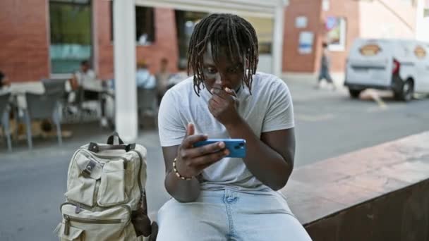Hombre afroamericano viendo el partido de fútbol en el smartphone celebrando en la terraza de la cafetería - Metraje, vídeo