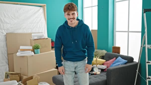 Fiatal spanyol férfi ül a kanapén, keresztbe tett kézzel, mosolyogva az új otthonra. - Felvétel, videó