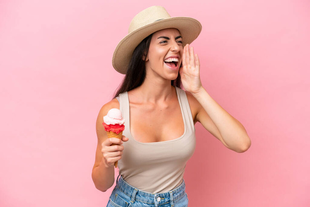 Giovane donna caucasica con un gelato alla cornetta isolato su sfondo rosa gridando con la bocca spalancata a lato - Foto, immagini