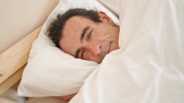 Hombre de mediana edad sonriendo confiado acostado en la cama en el dormitorio - Metraje, vídeo