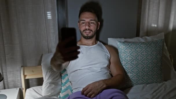 Junge arabische Mann tun Videoanruf sitzt auf dem Bett im Schlafzimmer - Filmmaterial, Video