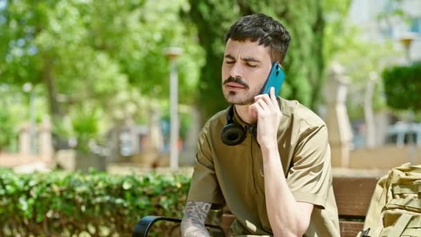 Молодий іспаномовний чоловік турист розмовляє по смартфону, сидячи на лавці в парку
 - Кадри, відео