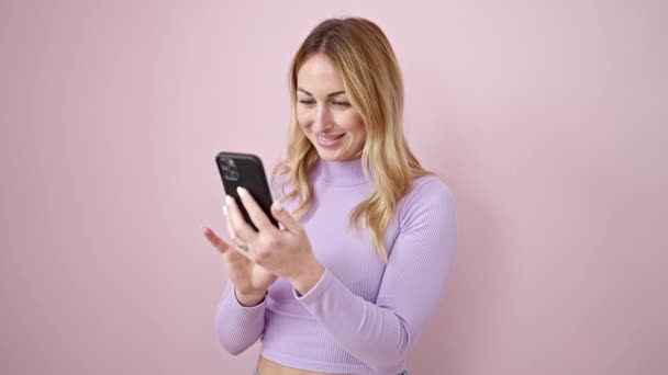 Jonge mooie Spaanse vrouw met behulp van smartphone glimlachen over geïsoleerde roze achtergrond - Video